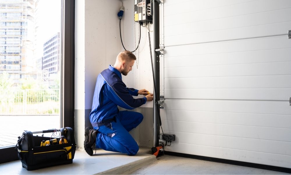 Pracownik w niebieskim kombinezonie montujący zamek automatyczny do bramy przesuwanej w garażu