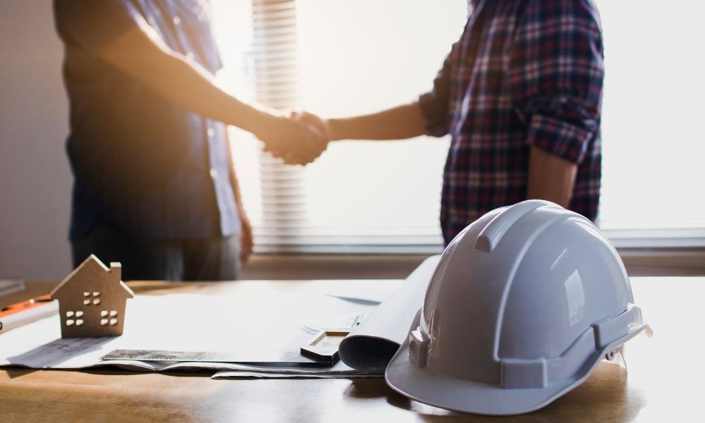 zdjęcie montera oraz klienta ściskających sobie dłoń, na sole leżą rysunki oraz kask budowlany