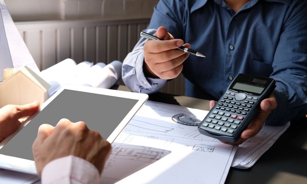 dwie osoby siedzące przy papierach architekta oraz z kalkulatorem i tabletem